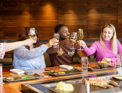 Three people clink glasses at a restaurant table with food in front of them, toasting and smiling.