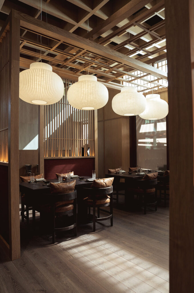 A restaurant dining area with wooden furnishings, pendant lights, and set tables with glassware and napkins.